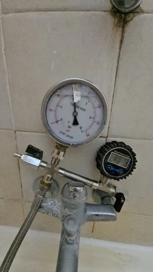 בדיקת לחץ על ברז אמבטיה בקיר עם סימני רטיבות ועובש בפוגות