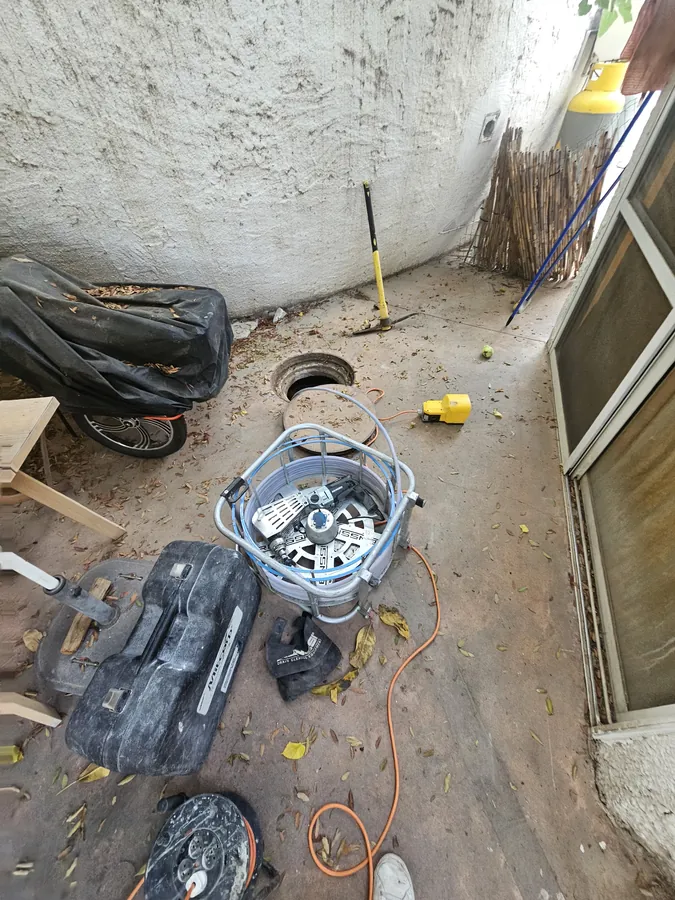 מכונת שטיפה בלחץ ומצלמת צינורות ערוכות ליד שוחת ביוב פתוחה בחצר הבית