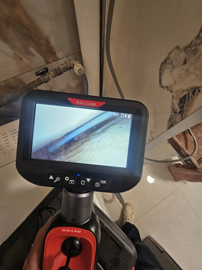 מצלמה אנדוסקופית ידנית בודקת צינור ניקוז מאחורי מכונת כביסה