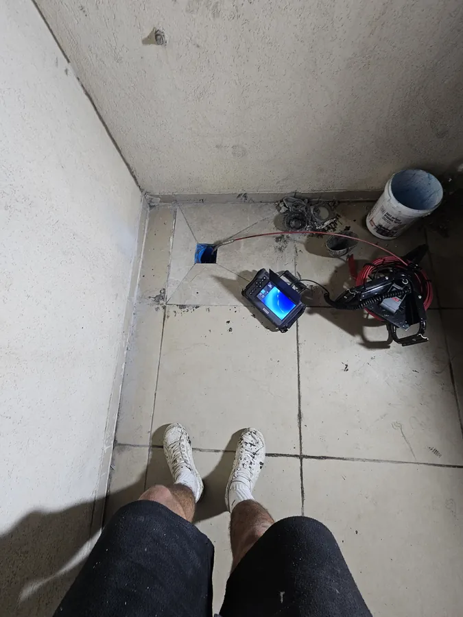 מצלמת צנרת מוכנסת דרך מחסום רצפה במקלחת, גליל הכבל והמסך על הרצפה