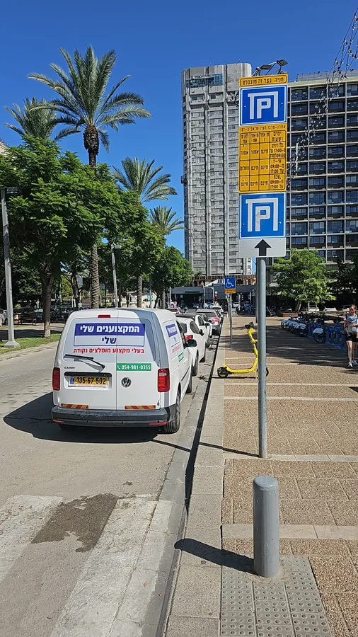 רכב השירות של המקצוענים שלי חונה ברחוב, עם מספר הטלפון 054-9810355 על הדלת האחורית