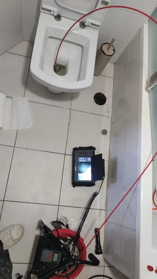 צילום קו ביוב דרך האסלה עם מצלמת צנרת, גליל הכבל והמסך על הרצפה